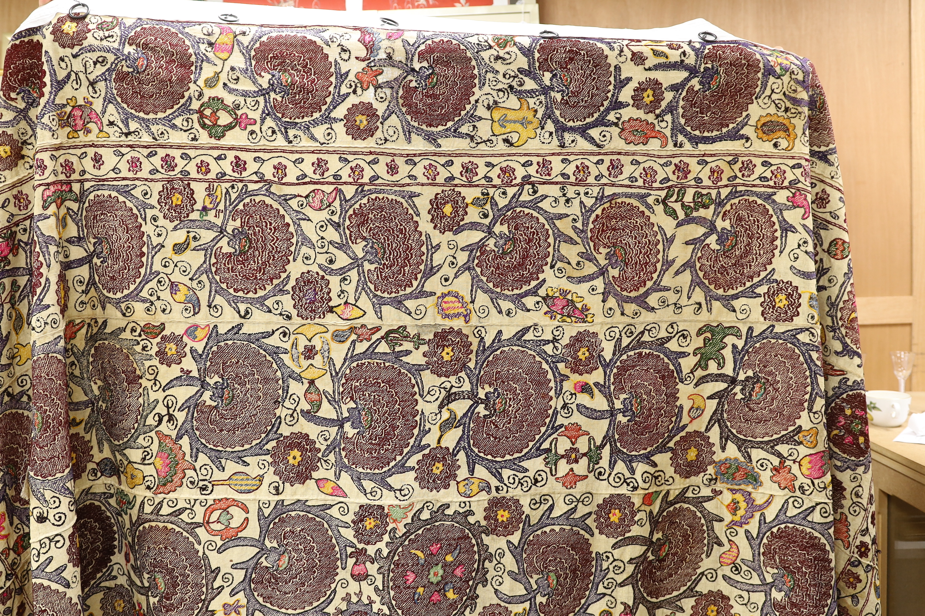 An exceptionally large Suzani hanging, embroidered with rows of stylised aubergine flower heads, the field filled with further polychrome flowers and serrated edged leaves, 190 x 270cm